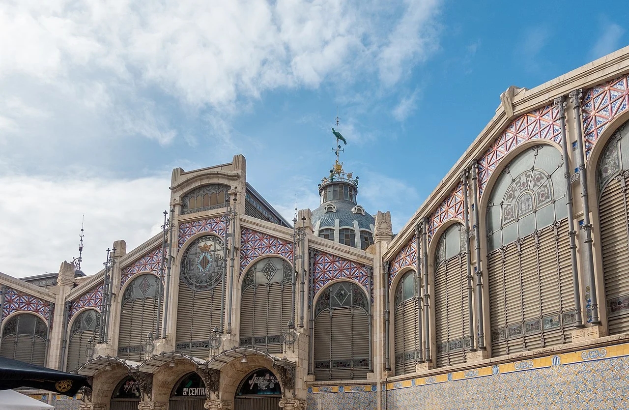 Фасад Mercat Central de València с керамической плиткой, центральной куполой 30 м с веткой-флюгером в виде попугая-cotorra и арочными окнами модернизма