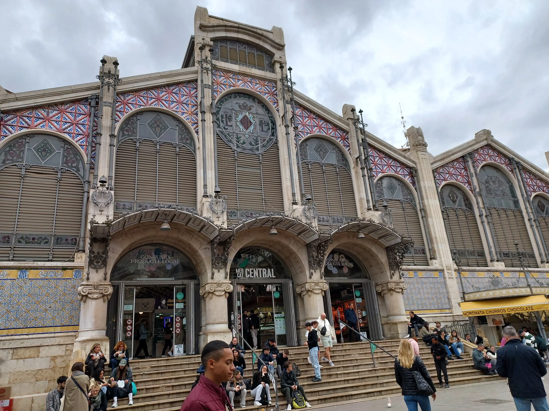 Главный фасад Mercat Central de València с керамическим тренкадис и арочными окнами на Plaza Ciudad de Brujas